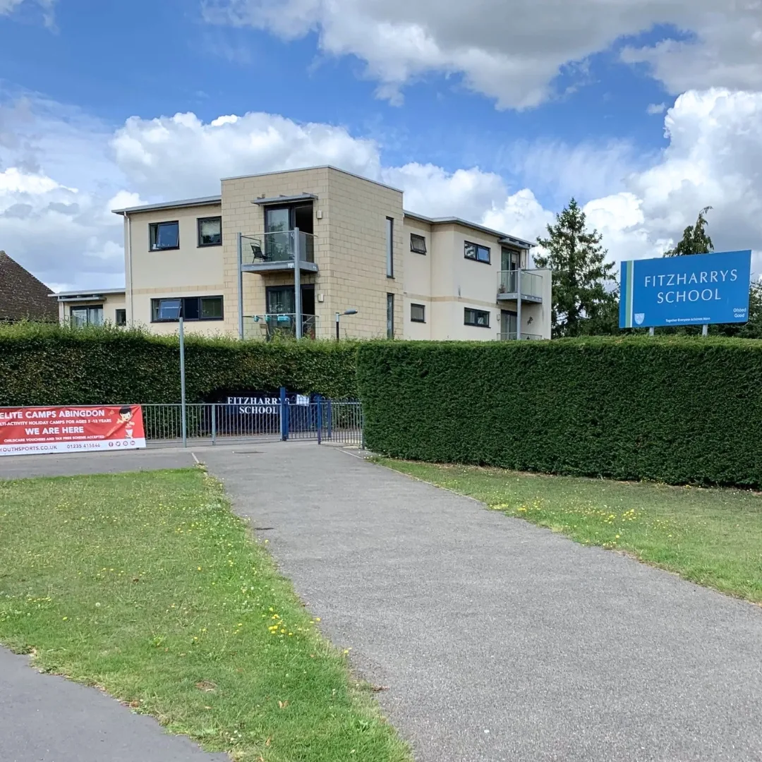 Fitzharrys School building behind a hedge, with the school sign on the right and an Elite Camps Abingdon banner by the gate