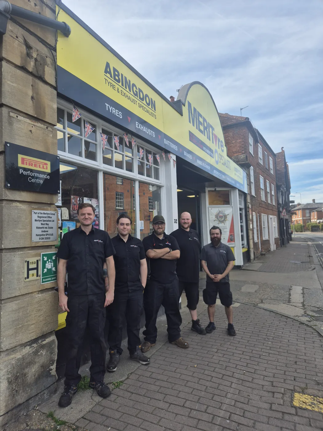 Five members of the Merityre Abingdon team in black work uniforms standing on the pavement in front of the yellow Merityre shopfront on Ock Street